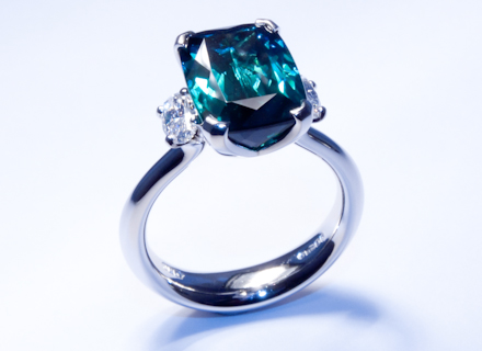 Four claw three stone platinum ring with a cushion cut indicolite tourmaline and oval diamonds