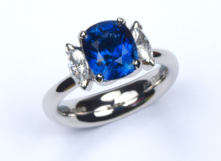 Four claw three stone platinum ring with a cushion cut blue sapphire and marquise cut diamonds